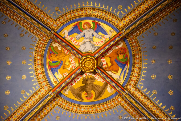 Painted rib vault with gilded central boss, four winged symbolic figures, inscription bands, stars, and multicolored ornament.
