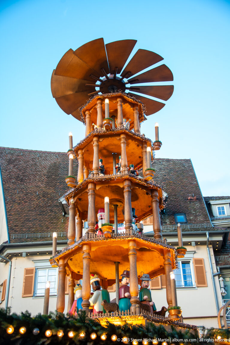 Large multi-tiered wooden Christmas pyramid with carved figures, candle-like lights, turned supports, and broad rotor blades.