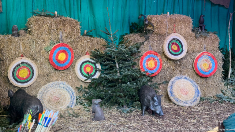 Colorful round archery targets on straw bales with boar figures, evergreen branches and arrows.