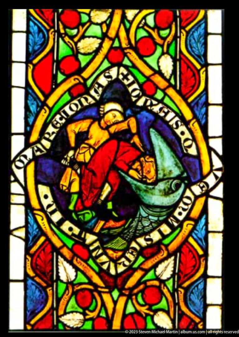 Medieval stained-glass medallion with robed figure pushed toward a large fish, surrounded by inscription band and colorful foliage.