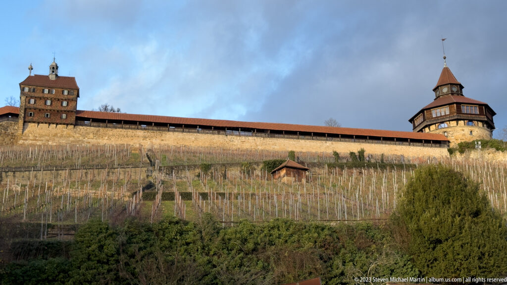 Esslinger Burg wall and towers extending across a hillside above rows of winter vineyard vines.