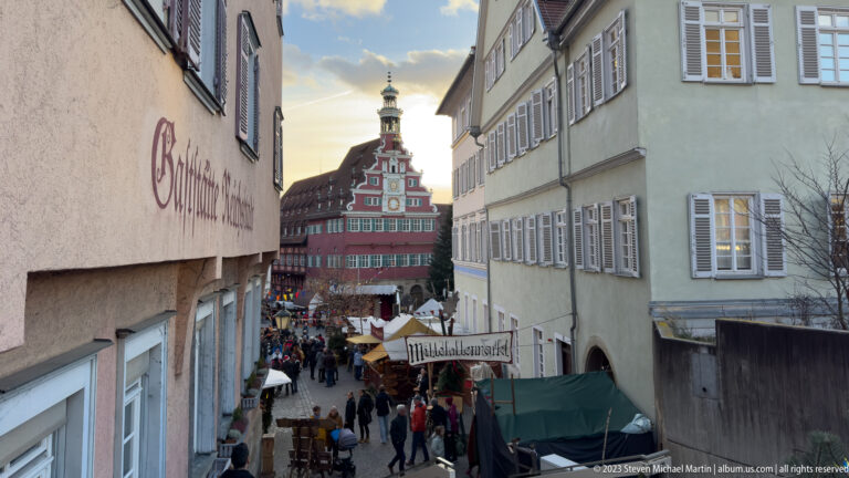 Crowded medieval-market street descending toward Esslingen's red Altes Rathaus, with a Mittelaltermarkt sign over the stalls.