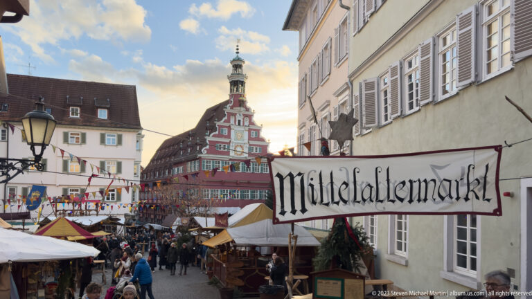 Mittelaltermarkt sign above crowded stalls, with Esslingen's red Altes Rathaus and clock tower in the background.