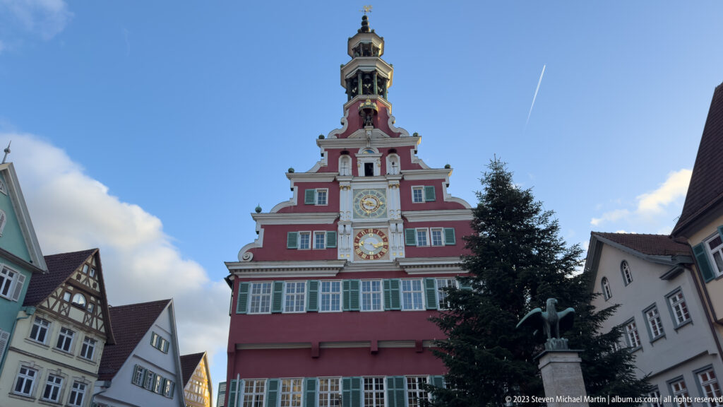 Frontal view of Esslingen's red Altes Rathaus with clocks and bell tower, flanked by historic old-town buildings.