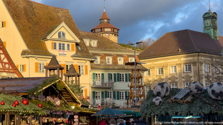 Christmas market decorations and stalls beneath colorful historic buildings, tiled roofs, a round tower, and green-patinated cupola.