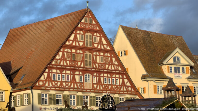 Large steep-gabled half-timbered house with red framing and white infill beside pale plastered buildings in Esslingen.