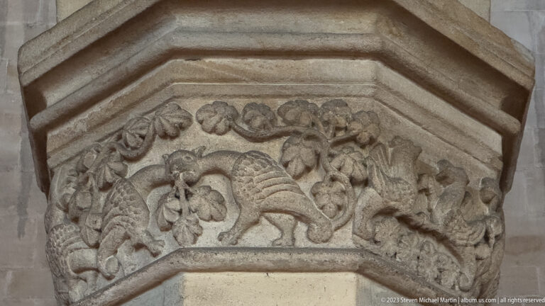 Close view of a weathered stone capital carved with curling foliage and a central animal-like creature.