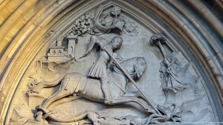Stone tympanum relief of Saint George on horseback spearing a dragon, with a standing female figure at right.