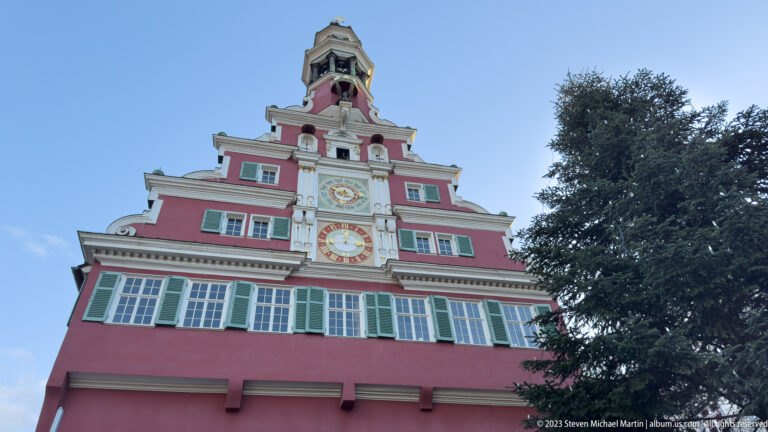 Upward view of Esslingen's red Altes Rathaus with green shutters, clock faces, stepped gable and bell tower.