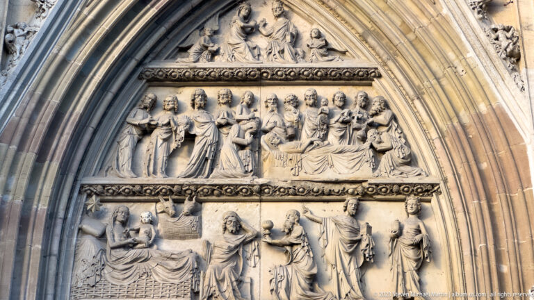 Carved stone church tympanum with several horizontal registers of seated and standing figures beneath concentric pointed arches.