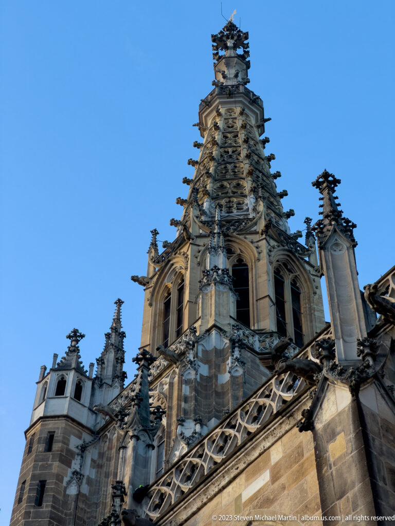 Low-angle close view of the ornate Frauenkirche tower with openwork tracery, pinnacles, buttresses, and arched openings against blue sky.