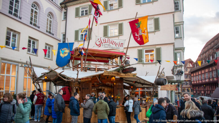 Busy wooden Glühwein stall decorated with flags and greenery, surrounded by winter visitors in Esslingen’s Christmas market.