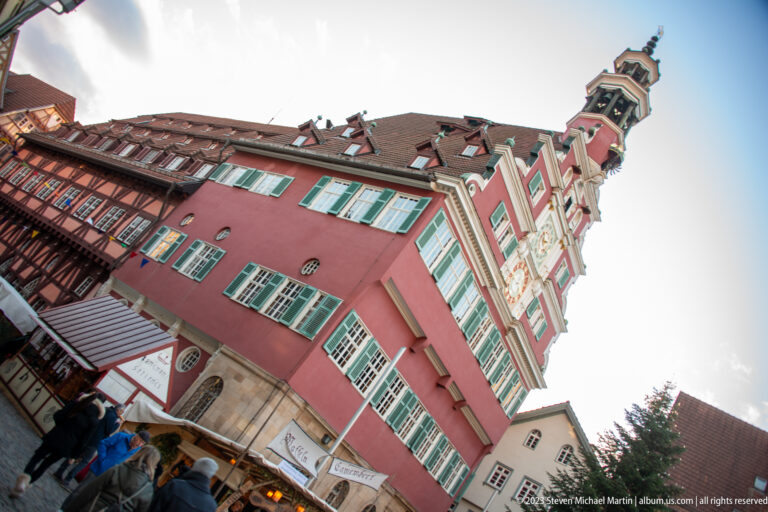 Dramatic tilted low-angle view of the red Altes Rathaus with green shutters, stepped clock gable, and ornate roof lantern.