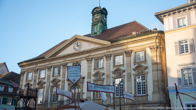 Formal pale-stone civic building with pediment clock, tall windows, sculpted surrounds, and green rooftop clock turret.