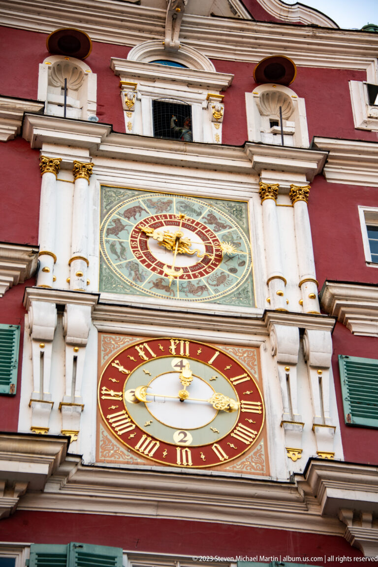 Close view of the Altes Rathaus clock façade with Roman-numeral clock below and ornate astronomical dial above.