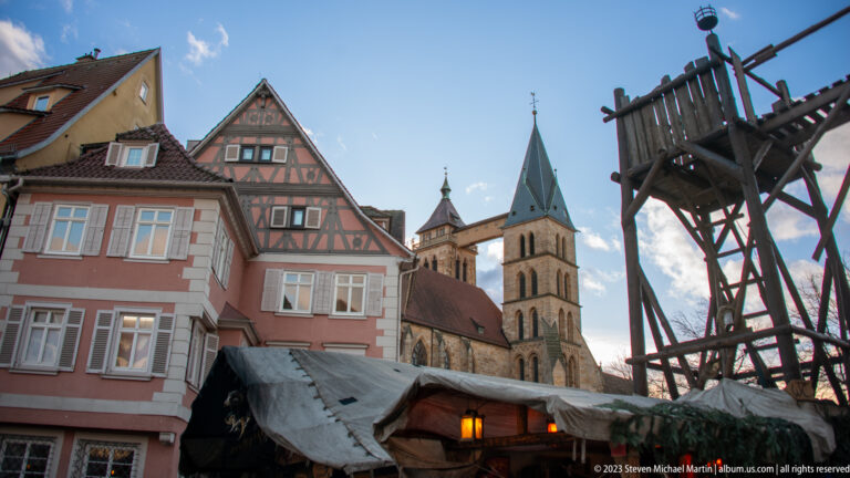Christmas market structures and historic gabled houses framing the twin towers and elevated connecting bridge of Stadtkirche St. Dionys.