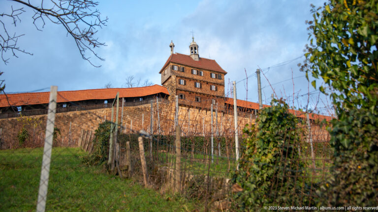 Esslinger Burg with long stone wall, covered red-tiled walkway, square tower, and winter-bare vineyard rows on the hillside.