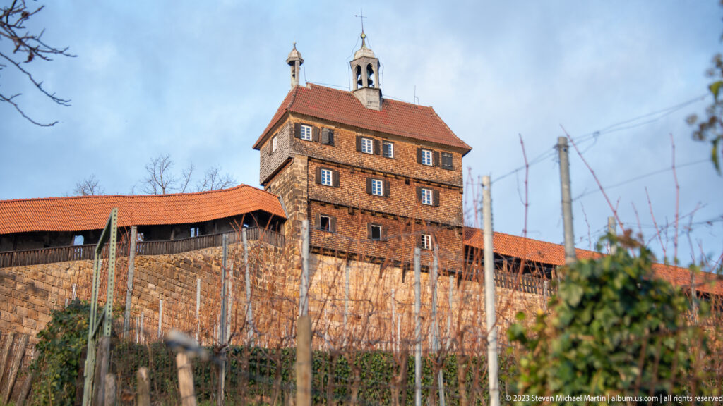 Square Esslinger Burg tower with timbered upper stories and red roof above stone walls and winter-bare vineyard rows.