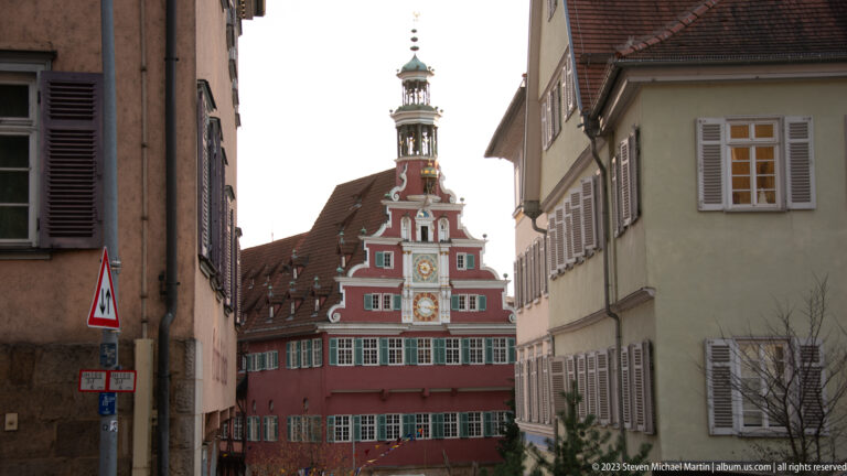 Altes Rathaus with red stepped gable and clocks framed by a narrow street between shuttered historic houses.
