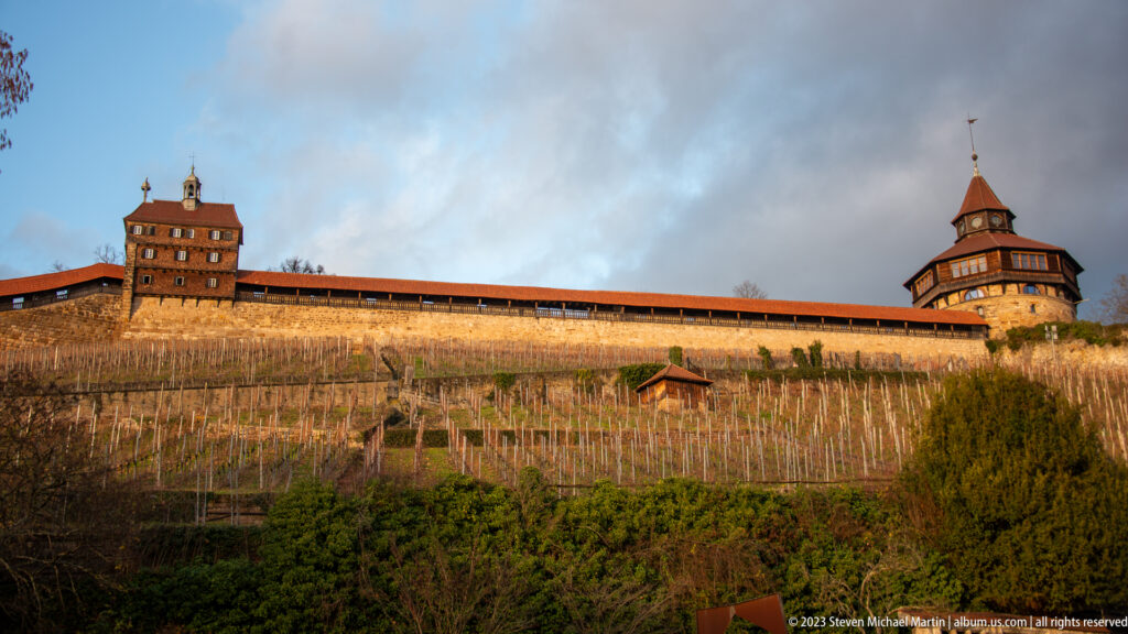 Long covered wall of Esslinger Burg linking square and polygonal towers above a steep winter vineyard.