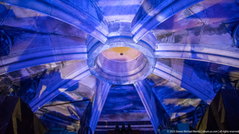 Upward view of massive stone ribs converging around a circular opening inside Freiburg Minster tower.