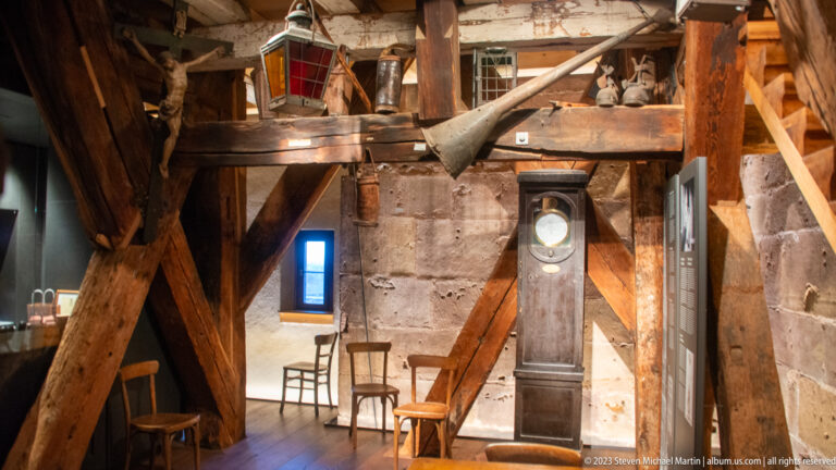 Timber-framed tower room with stone walls, tall clock case, chairs, and historic fittings inside Freiburg Minster.