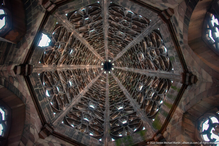 Upward interior view through the dense stone lattice and tracery of Freiburg Minster openwork spire.