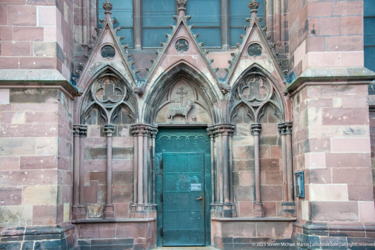 Green door beneath three pointed Gothic arches with carved tracery and red sandstone on Freiburg Minster.
