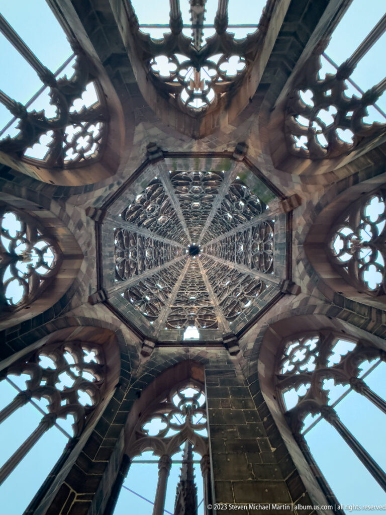 Wide upward view inside Freiburg Minster’s tower, with converging ribs, pointed windows, and pierced stone tracery.