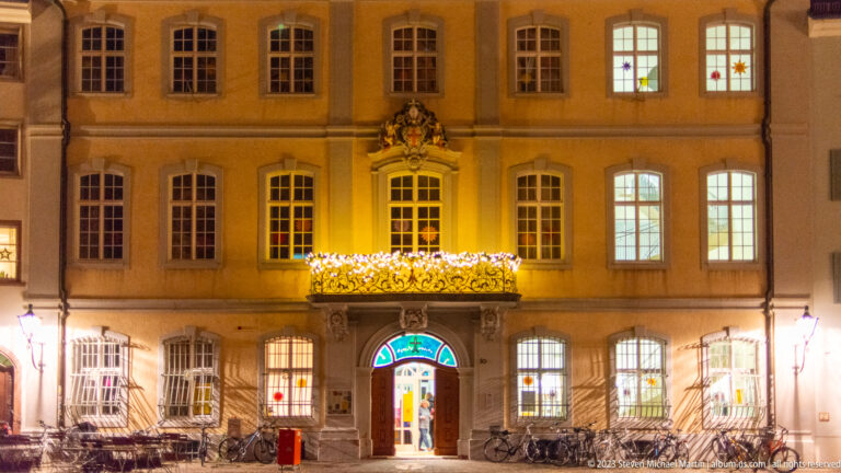 Symmetrical historic Freiburg façade with central doorway, decorative crest, festive lights, and bicycles parked outside.