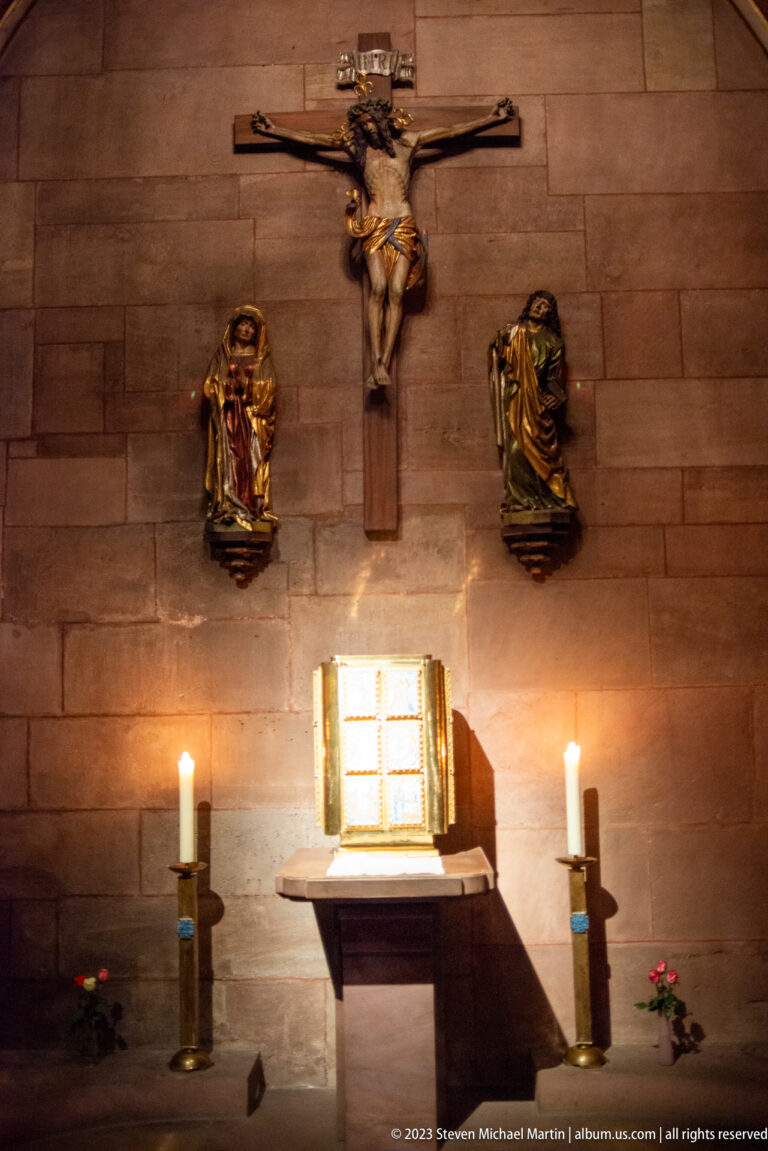 Crucifix above a small shrine with two gilded sculptures and candles inside Freiburg Minster.
