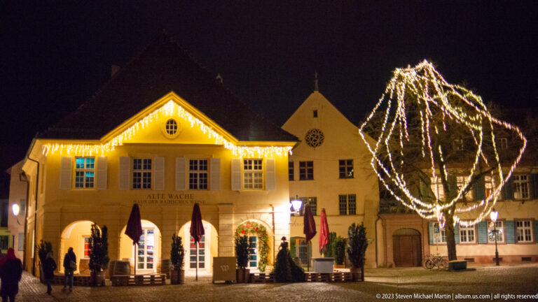 Alte Wache on Münsterplatz illuminated with roofline lights and a large glowing Christmas ornament in front.