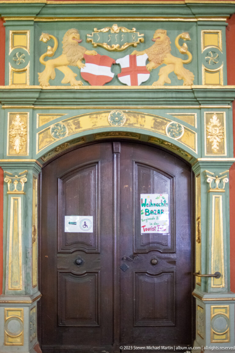 Dark wooden double doors framed by gilded heraldic decoration, painted lions, and an arched historic surround.