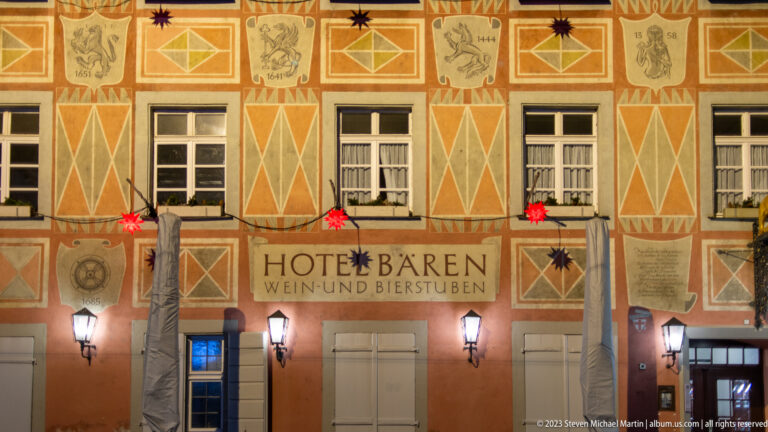 Painted Hotel Bären façade with geometric motifs, central German sign, wall lanterns, and red Christmas stars.