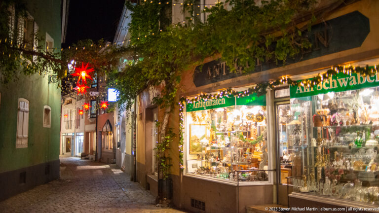Bright traditional shop window filled with ornaments beside a narrow cobbled lane decorated with red Christmas stars.