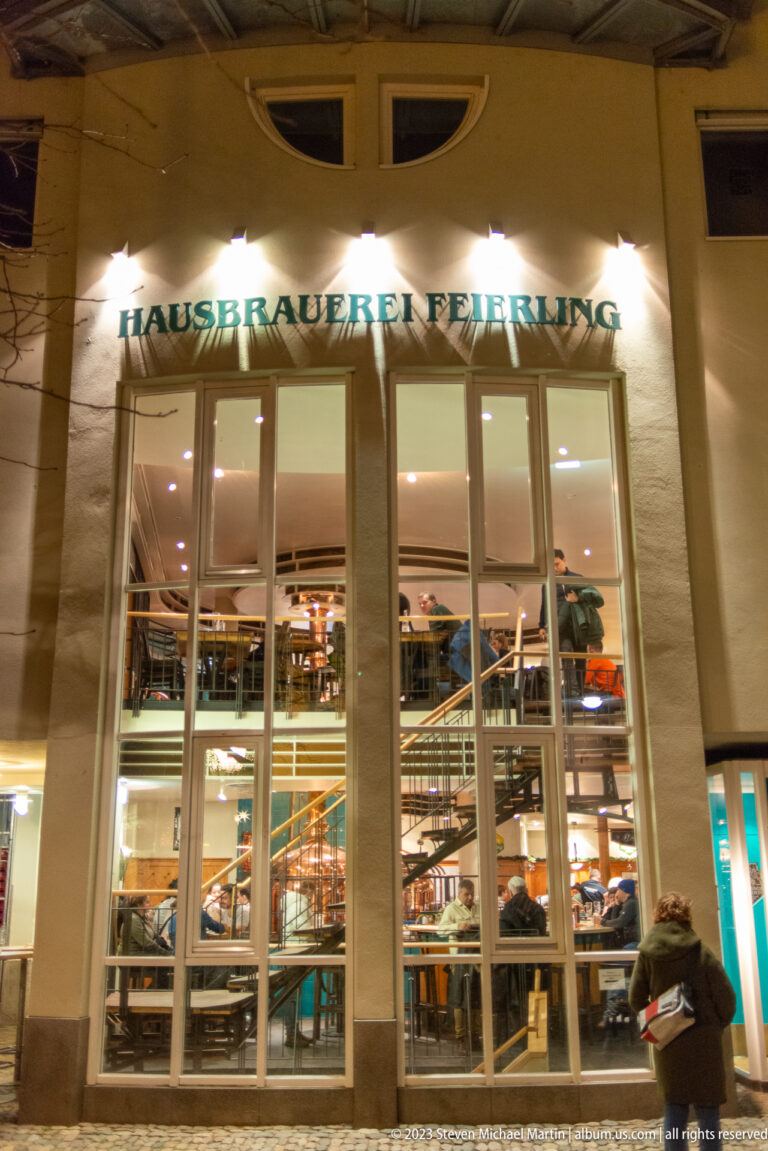 Night exterior of Hausbrauerei Feierling with its name above tall windows and a brightly lit multi-level interior.
