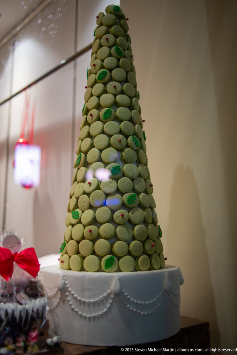 Cone-shaped Christmas tree made from pale green macarons with small red and green accents on a white pedestal.