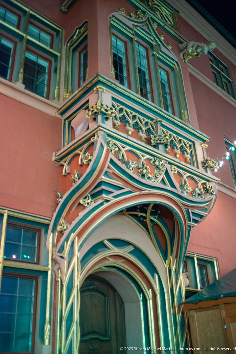Low-angle view of an ornate painted balcony with carved supports above a historic Freiburg doorway.