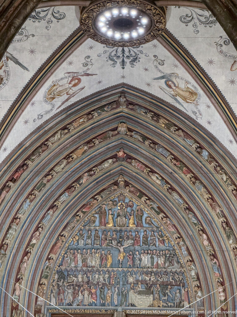 Close upward view of Freiburg Minster portal with densely carved Gothic tympanum, layered archivolts, and a circular light above.