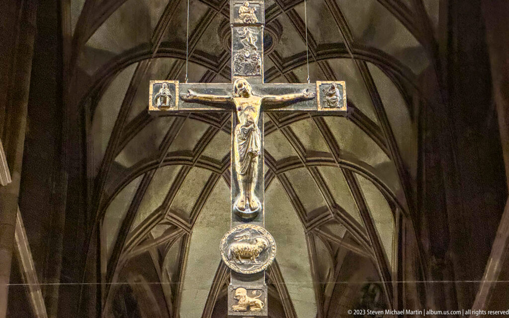 Large illuminated crucifix hanging before dark ribbed Gothic vaults inside Freiburg Minster.