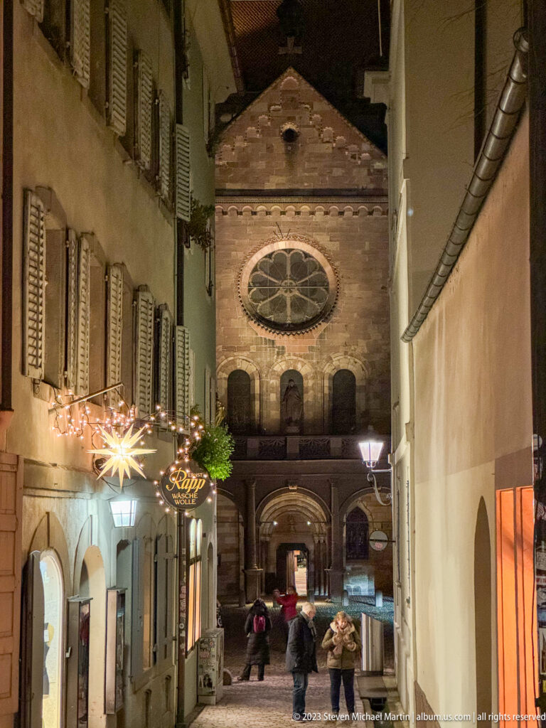 Narrow Freiburg lane ending at a church facade with rose window and arched entrance, beneath Christmas star lighting.