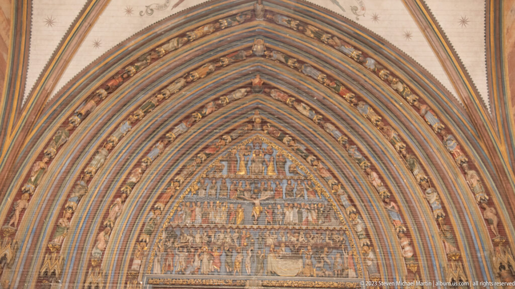 Painted Gothic tympanum filled with rows of figures and framed by layered pointed archivolts.