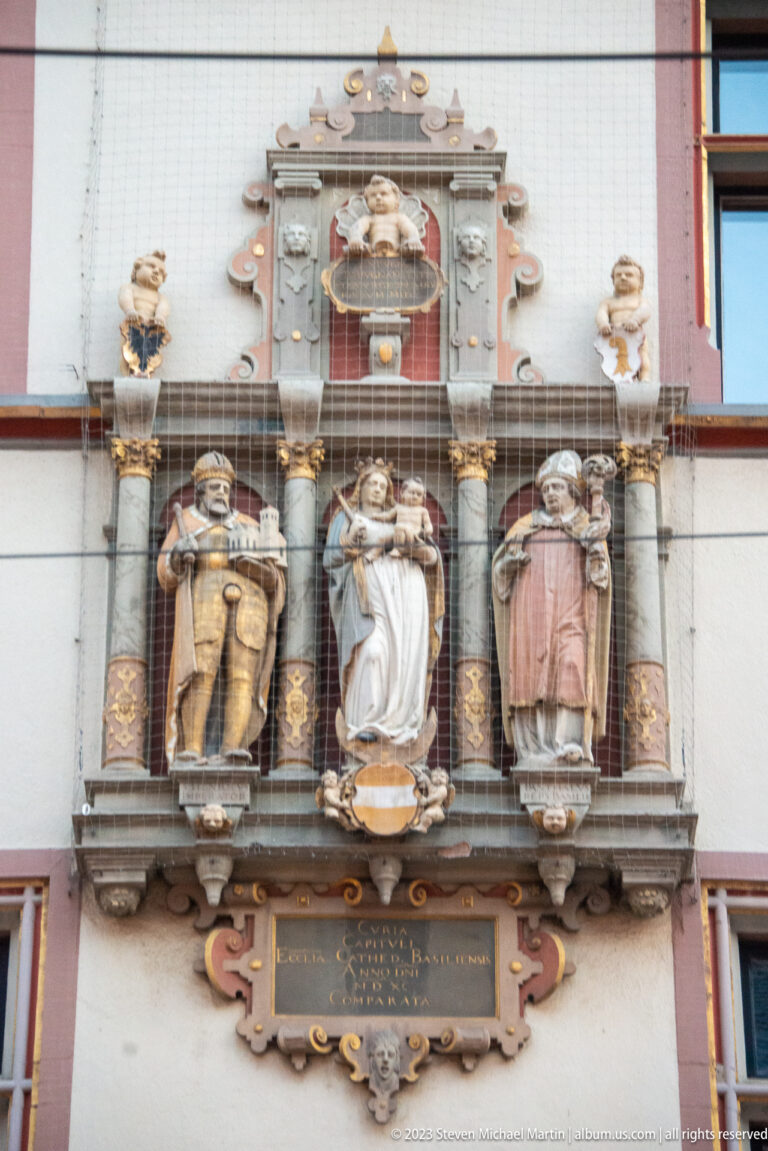 Three standing sculpted figures in ornate niches beneath carved architectural decoration on a historic Freiburg façade.