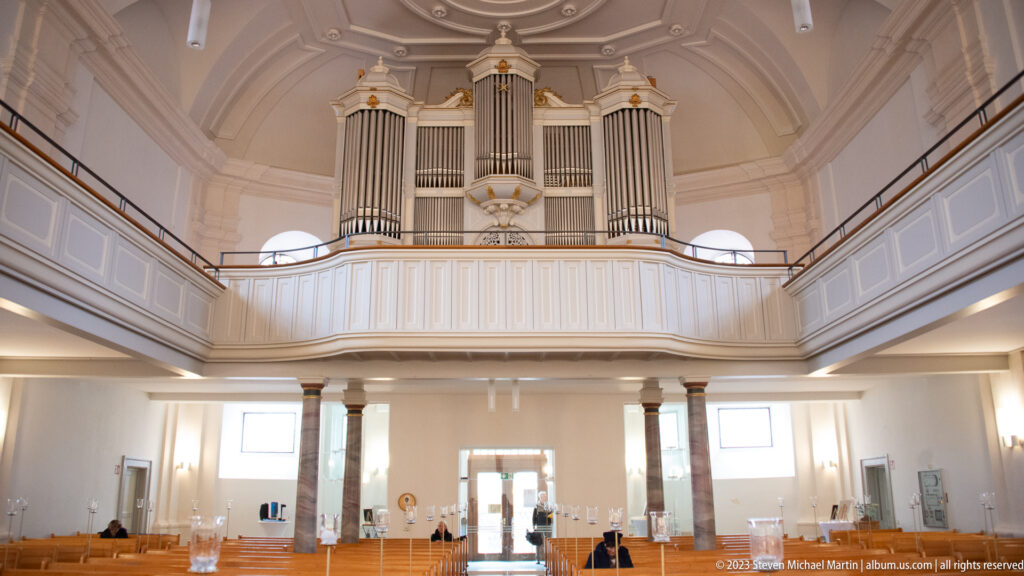 Large pipe organ with three principal pipe towers above a white gallery in a bright church interior.