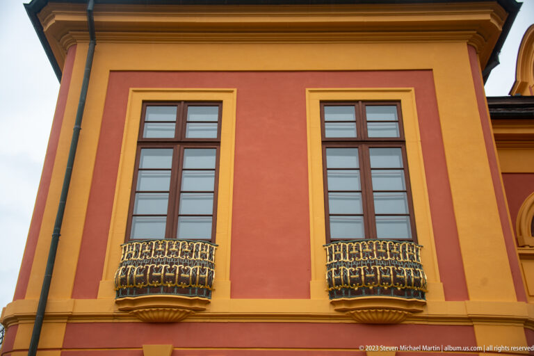 Two tall windows with small gilded iron balconies on a red-and-ocher Schloss Favorite façade.