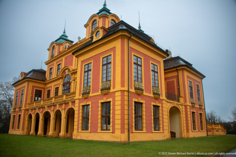 Oblique view of red-and-ocher Schloss Favorite with arcades, tall windows, corner pavilions, and green-capped roof towers.