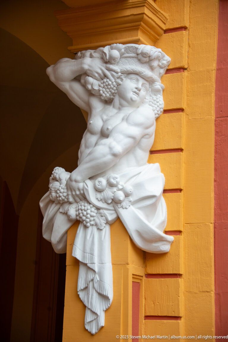White sculpted half-figure with drapery and decorative attributes projecting from an ocher pier at Schloss Favorite.