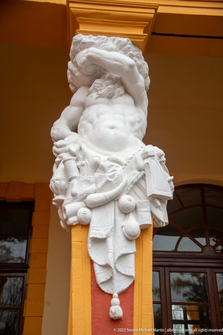White bearded half-figure with drapery and clustered decorative attributes on an arcade pier at Schloss Favorite.