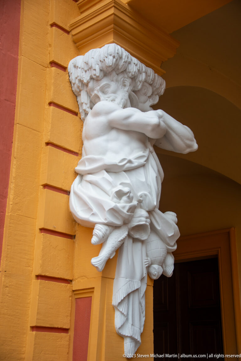 White female half-figure with drapery and fruit-like bundle projecting from an arcade pier at Schloss Favorite.