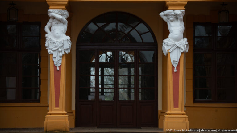 Dark glazed arched doorway between ocher piers topped by white figural brackets at Schloss Favorite.